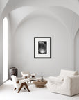 'Strength Feather' – a black and white art print presented in a black frame, shown in a minimalist living room.