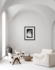 Framed white feather on a black background hanging on a white wall.