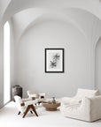 Black and white framed photograph of two seed pods hanging on a wall in an all-white minimalist contemporary style living room.