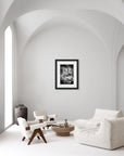 Framed black and white photograph of dandelion seeds mid flight hanging on an all-white wall in an all-white living space.