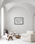 Framed white feather hanging on a wall in an all-white contemporary living space.